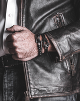 A close-up of a person wearing a black leather motorcycle jacket over a white button-down shirt, with a beaded bracelet and watch on the wrist.