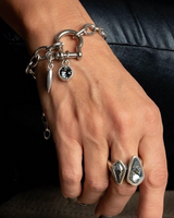 Hand wearing a silver bracelet with charms and two rings on a dark background