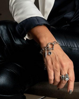 Person wearing multiple bracelets and rings on a dark background