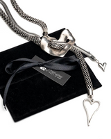 A silver-toned braided snake chain necklace with a heart-shaped clasp and two dangling heart charms, displayed on a black velvet gift pouch with a black ribbon and a WhiteWise tag.