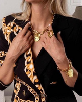 Person wearing gold jewelry with a black blazer and patterned scarf.