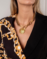 Person wearing a gold chain necklace with a pendant, black blazer, and patterned top.