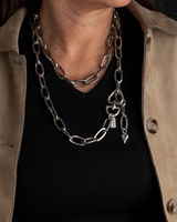 Person wearing a chain necklace with a beige jacket and black shirt.