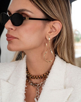 Woman wearing gold hoop earrings and sunglasses with a blurred background