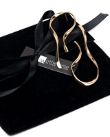 Gold earrings on a black velvet surface with a visible brand tag.