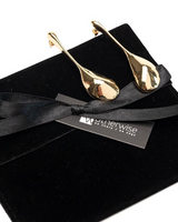 Gold teardrop-shaped earrings on a black ribbon with a 'outerwise' tag on a black box.