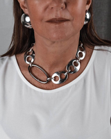 Chunky silver-plated anchor link necklace worn with matching oversized earrings on a model in a white top.