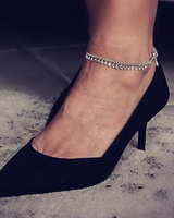 Dainty 999 silver antique plated anklet with round charms, worn on a bare ankle, paired with black high heel shoe.