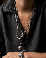 Person wearing a long silver chain necklace and bracelet against a dark background