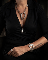Person wearing a silver necklace and bracelet with a dark background