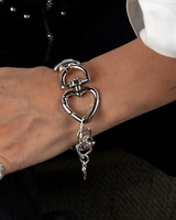 Silver bracelet with heart and key design on a wrist against a dark background