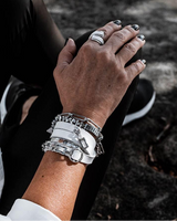Close-up of a person's hand with multiple silver bracelets and rings on a natural background