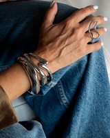Three chunky silver cuff bangles stacked on a wrist, paired with a silver ring, showcasing a modern, sleek design.
