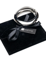 Chunky silver cuff bangle resting on a black suede pouch, featuring a sleek, polished finish and a ribbon tie.