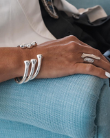 Silver plated open bangle cuff worn on a wrist, featuring a sleek design with three curved elements, paired with a chunky ring.