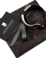 Unisex leather wrap bracelet featuring a silver o-ring metal cuff, displayed on a dark suede gift pouch.