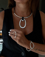 Leather circle pendant choker features a large brass pendant with a silver-plated finish, worn with a structured black outfit.