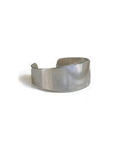 Chunky minimalist metallic cuff bracelet featuring a wide flat design in shiny rhodium-plated brass, adjustable fit.