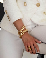 Chunky gold cuff bangles stacked on a model's wrist, paired with a white textured blazer and ring, exuding an elegant style.