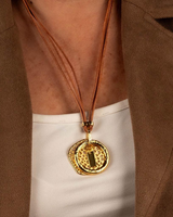 Natural leather strands with a hammered golden hoop pendant, worn on a model over a white top, showcasing an edgy design.