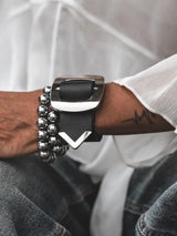 Wide black leather cuff bracelet featuring a large silver buckle with a pointed design, worn on a wrist alongside a beaded bracelet.