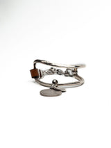 Brown leather wrap bracelet featuring oversized silver-plated horse bit links and coin pendants, adjustable clasp.