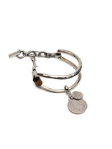 Brown leather wrap bracelet featuring oversized silver-plated horse bit links and two hanging coin pendants.