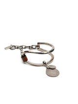 Brown leather bracelet with oversized silver-plated horse bit link and coin pendants, featuring a chunky cuff design.