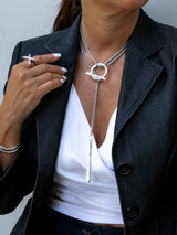 Person wearing a stylish silver necklace with a unique pendant, paired with a white top and dark jacket.