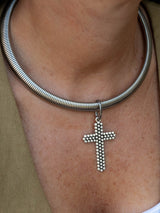 A close-up of a silver snake chain necklace worn on a person's neck, featuring a dangling cross pendant made of small silver beads.