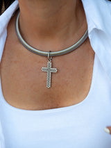 A close-up of a person wearing a silver snake-style choker necklace with a dangling cross pendant, paired with a white ribbed top.