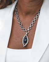 Bold black oval Murano glass pendant on a chunky stainless steel chain, worn with a white top and blazer.
