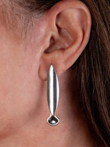 A close-up of a person's ear wearing a long, slender silver drop earring with a small circular detail at the bottom.