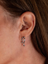 A close-up of a person's ear wearing a small abstract silver dangle earring.