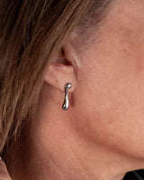 A close-up of a woman's ear wearing a small polished silver teardrop-shaped stud earring.