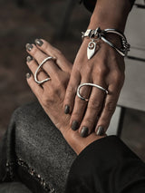 A close-up lifestyle shot of two hands resting on each other, showcasing a collection of silver-toned jewelry. The hands feature matte gray nail polish and are adorned with multiple silver rings, a heart-shaped pendant bracelet, and a chunky chain bracelet.