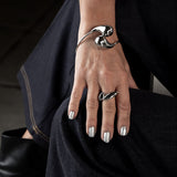 Close-up of a hand wearing a silver bracelet and ring, with black boots and pants in the background.