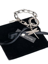 Chunky silver bracelet featuring a detailed dragonfly pendant on a heavy-duty link chain, displayed on a black suede pouch.