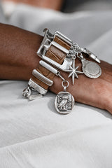 Chunky silver cuff bracelet featuring brown snake leather bands and five silver-plated charms, worn on a wrist.