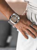 Textured beige leather buckle bracelet worn on a wrist, featuring a wide cuff and prominent silver buckle detail.
