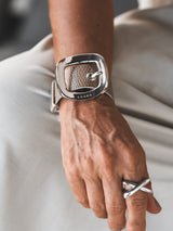 Textured beige leather wide cuff bracelet featuring a prominent silver buckle, worn on a hand with a silver ring.