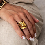 Hand wearing a gold ring with a textured design on a neutral background