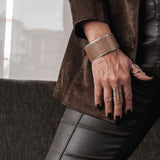 Wide brass bangle with beige animal print leather, featuring a textured design and adjustable open-cuff fit.