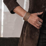 Wide brass bangle with beige animal print leather inlay, worn on a model's wrist, showcasing a bold and textured design.