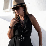 Woman wearing a black sleeveless top, beige hat, and sunglasses against a white wall.