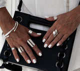 Four silver-plated adjustable chunky rings worn on hands, showcasing a mix of styles, paired with a black handbag.