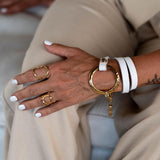 White leather triple wrap bracelet with a hammered gold loop and stainless steel chain, worn with matching rings.
