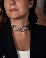 Chunky sculptural collar necklace in sterling silver plating, featuring oversized loops, worn as a modern statement choker.
