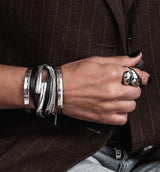 Layered leather and snake chain wraparound bracelet in black, featuring a silver bangle, stacked on a wrist with nails painted black.