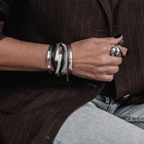 Layered black leather and silver snake chain bracelet, featuring a malleable silver bangle, worn stacked on wrist.